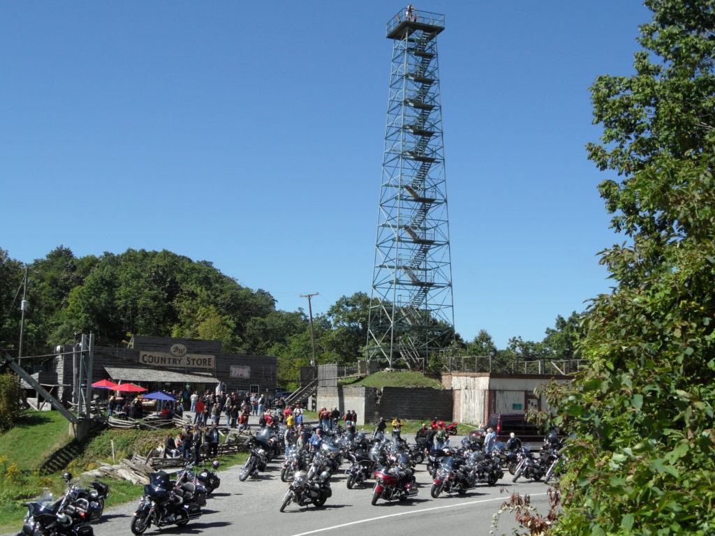 Numerous motorcycles are parked at Big Walker Lookout with the 100-foot lookout towering overhead.