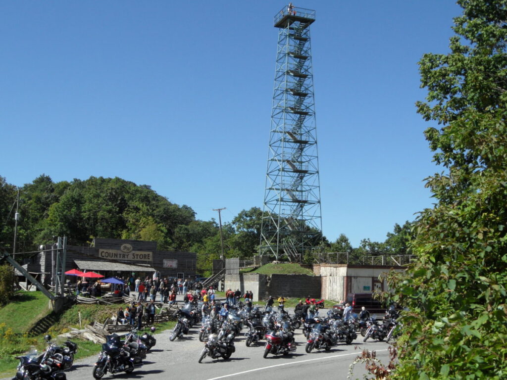 Numerous motorcycles are parked in the gravel lot in front of Big Walker Lookout's multistory tower.