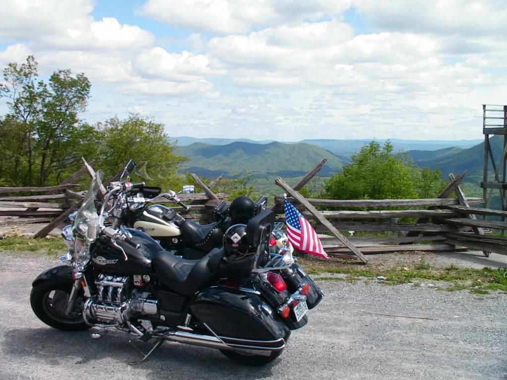 Motorcycles sit on the gravel surface at Big Walker Lookout with the forested mountains stretching off into the distance, meeting the cloud-filled sky.