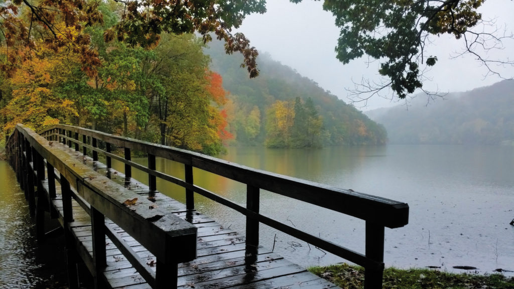 A bridge over a foggy lake leads to fall-colored trees on the opposite shore at Hungry Mother State Park.