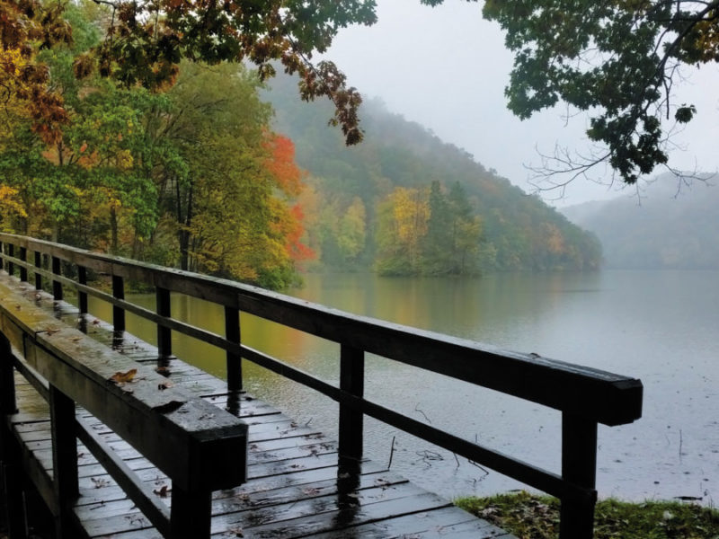 A bridge over a foggy lake leads to fall-colored trees on the opposite shore at Hungry Mother State Park.