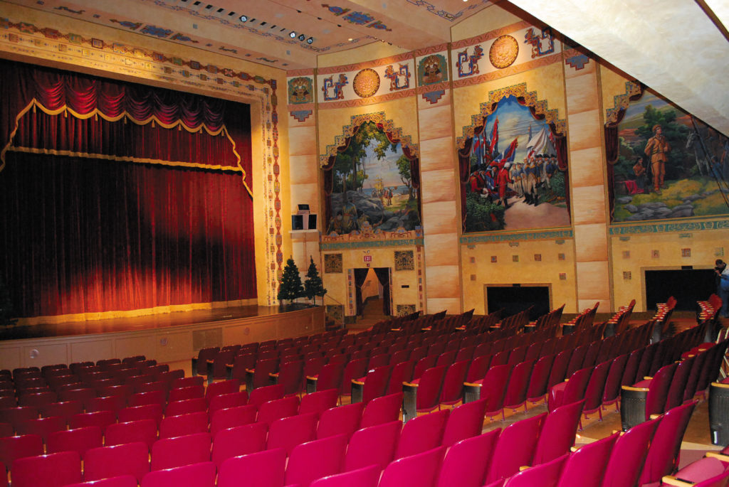 Red theater seats face the red-curtained stage in the Lincoln Theater in Marion, VA. Murals line the yellowish-gold walls.