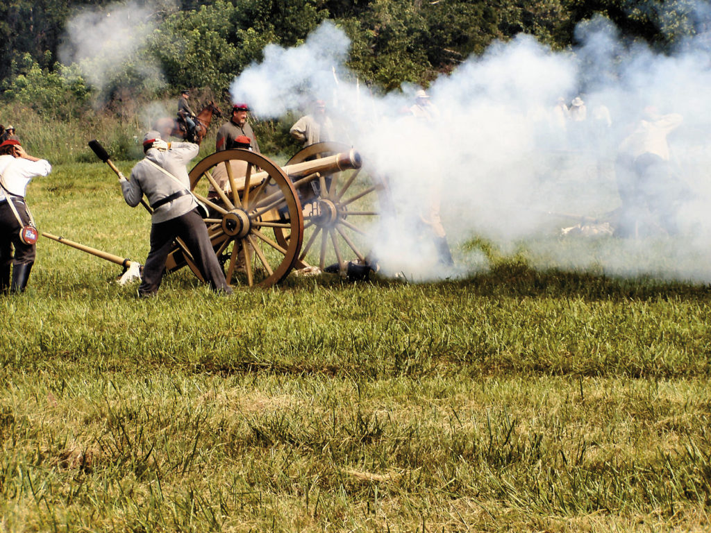 Uniformed men cover their ears while firing cannons, releasing billowing smoke over the grassy field at the Museum of the Middle Appalachians.