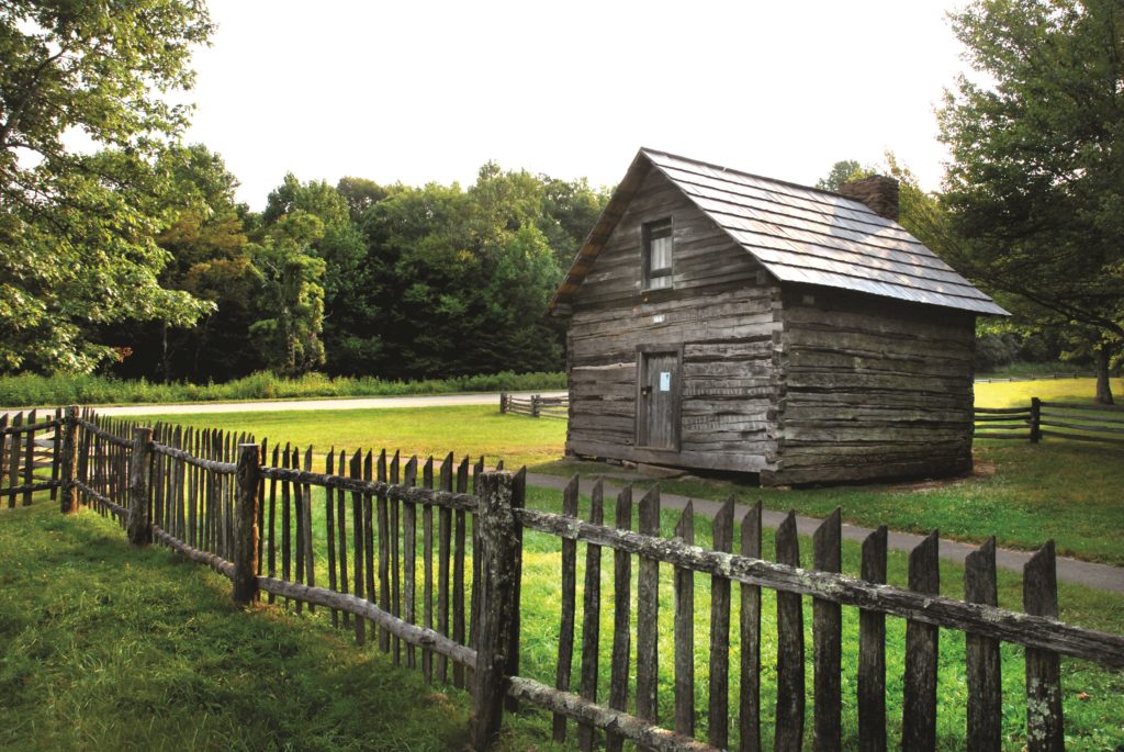 Historic Puckett log cabin sits just off the Parkway framed by hardwood forest and picket fences surrounding a green lawn.