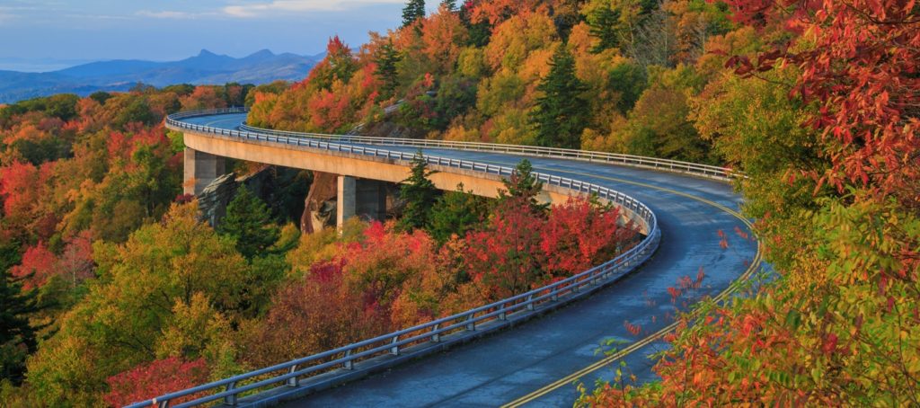 Linn Cove Viaduct curves along the side of Grandfather Mountain surrounded by fall foliage reds and oranges.