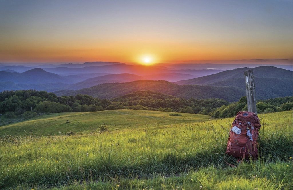a red backpack leans against a wooden post as the sun sets over the smoky mountains