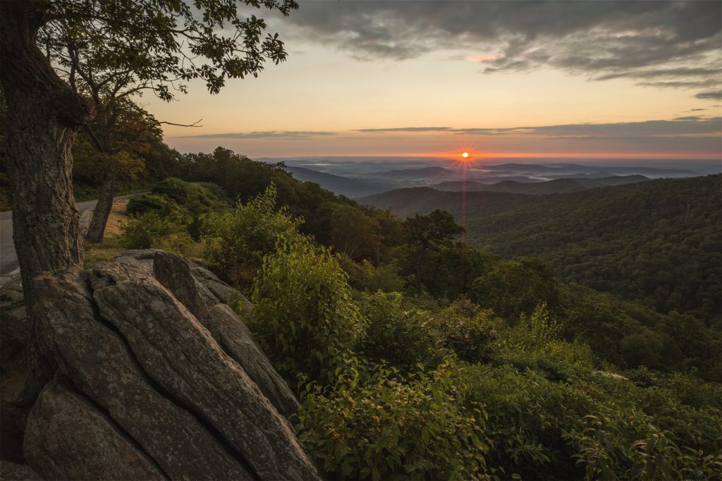 The sun sets over the distant valley below the rocky overlook on Skyline Drive offering this spectacular view.