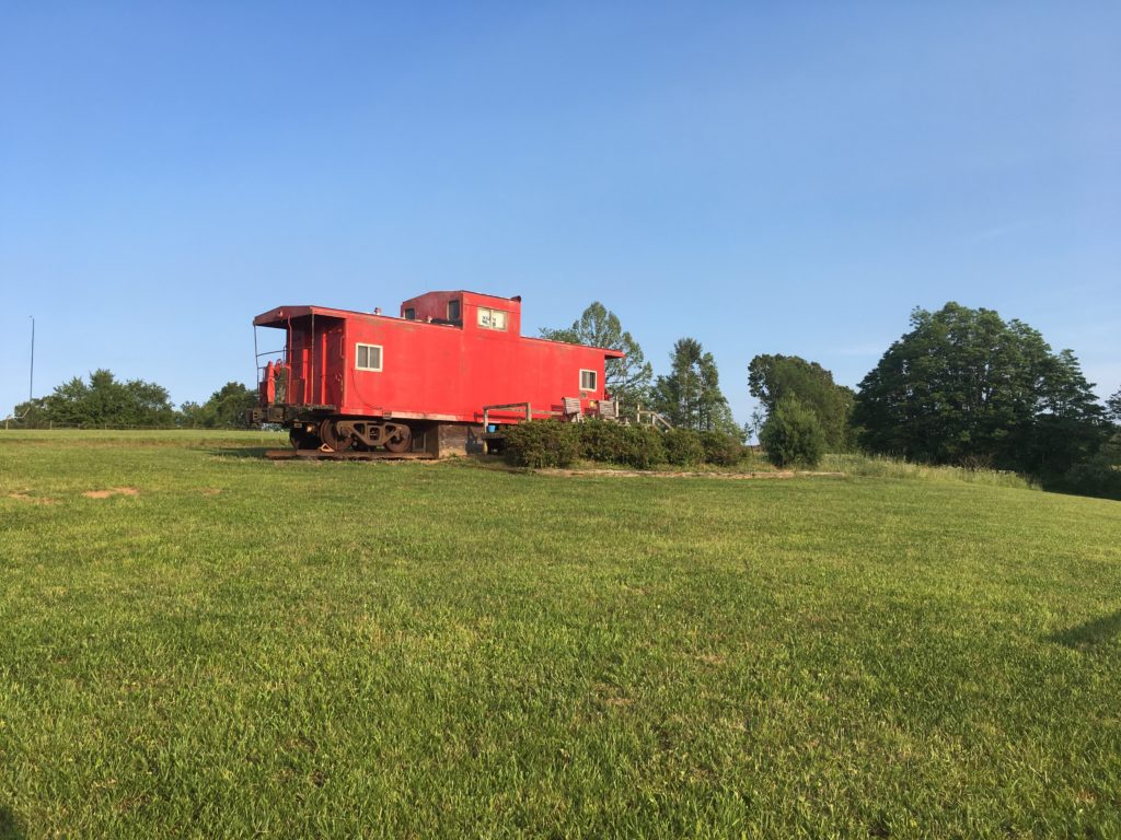 A red rentable caboose is surrounded by a grassy lawn and blue sky.
