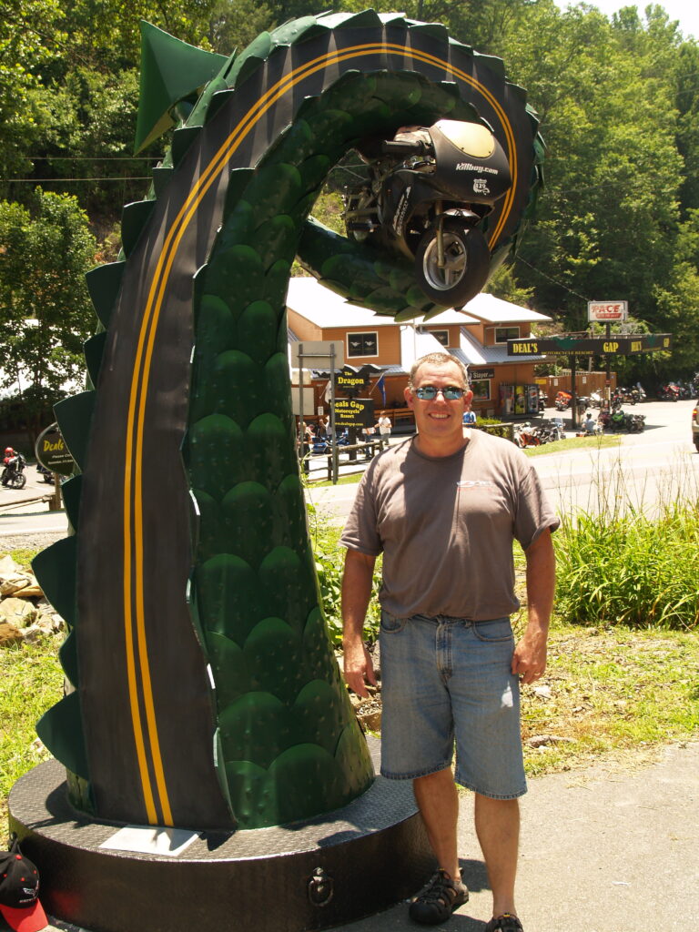 A sculpture of a dragon's tail with a road painted on it holds a motorcycle at the entrance to the Tail of the Dragon in Robbinsville, North Carolina.