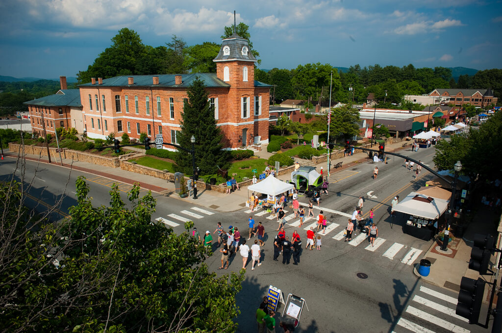 People gather on the street in Brevard for a downtown festival surrounded by historic buildings.