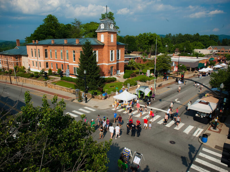 People gather on the street in Brevard for a downtown festival surrounded by historic buildings.