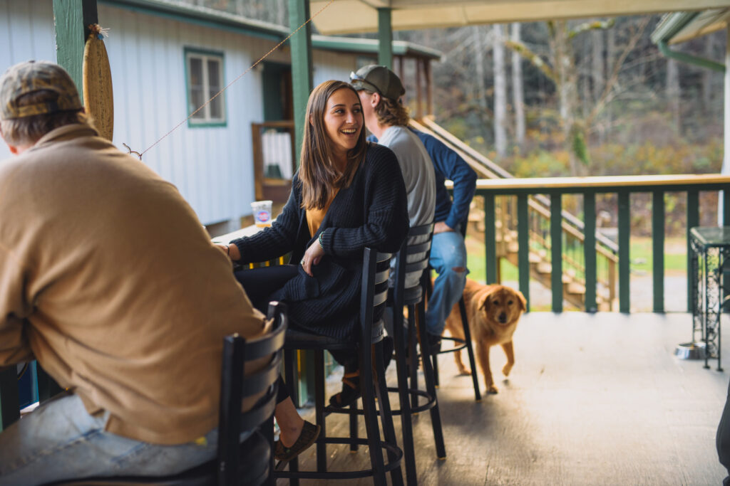 Patrons sit at a bar outside the Forks of the River Taproom with a dog in the background.