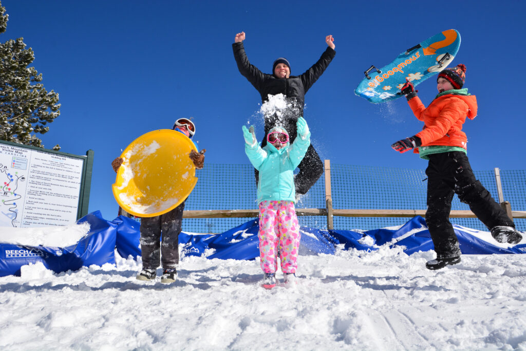 Joyful children stand at the top of a sledding hill with their sleds.
