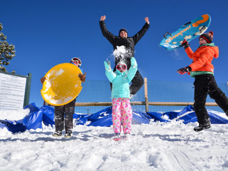 Joyful children stand at the top of a sledding hill with their sleds.