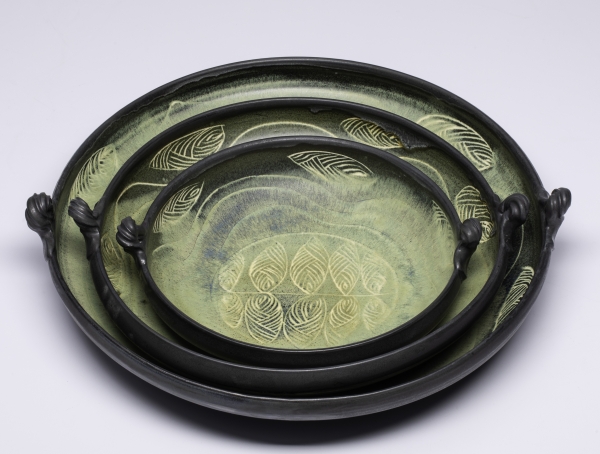 Green stacked pottery serving dishes with etched leaves.