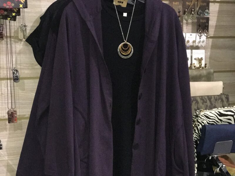 A purple women's sweater hangs over a black shirt and necklace in a store.