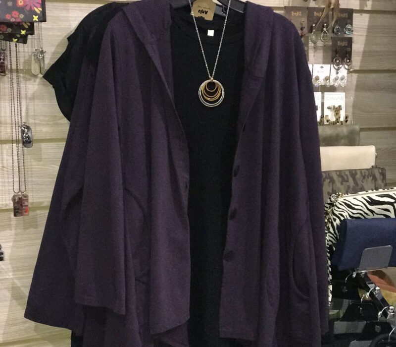 A purple women's sweater hangs over a black shirt and necklace in a store.