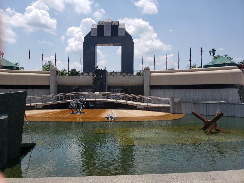 The National D-Day Memorial's arch overlooks a reflecting pool with statues of soldiers attempting to climb the beach amid landmines.