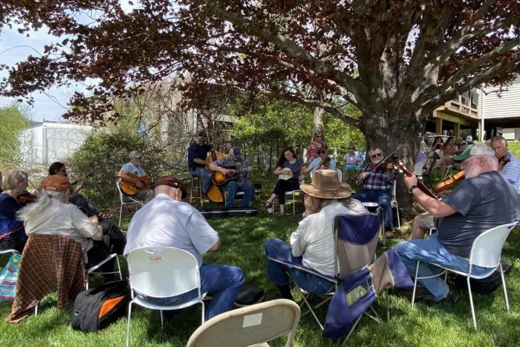 Musicians sit in a circle under a tree at the Floyd Country Store Sunday Music Jam.