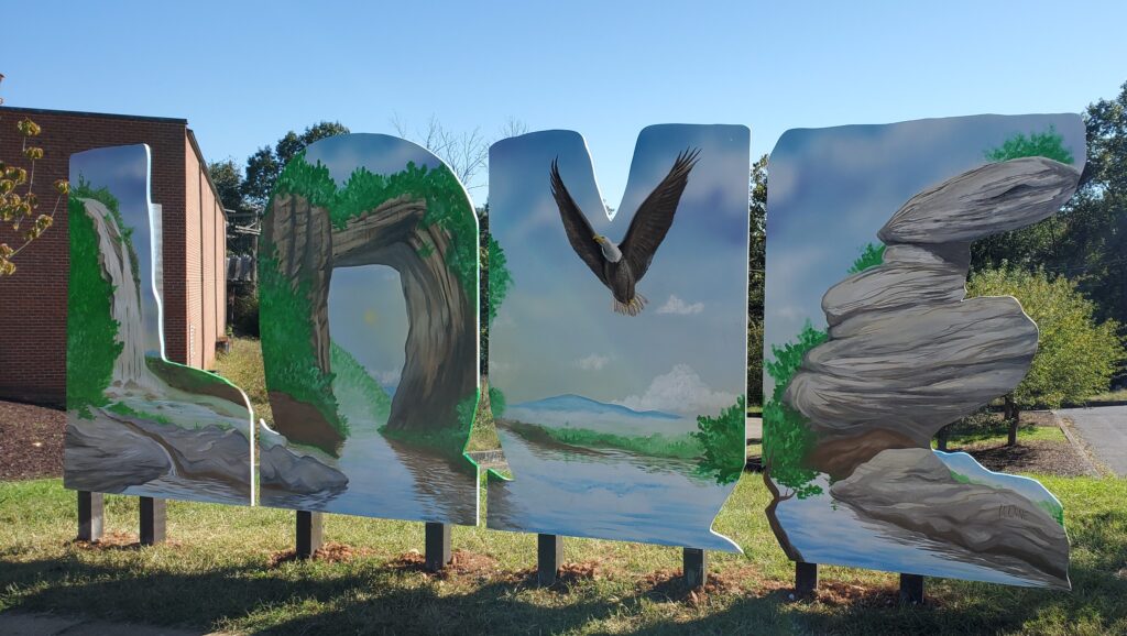 The L-O-V-E sign at Lexington & Rockbridge County includes a waterfall, eagle, the Natural Bridge Arch and a rocky cliff.