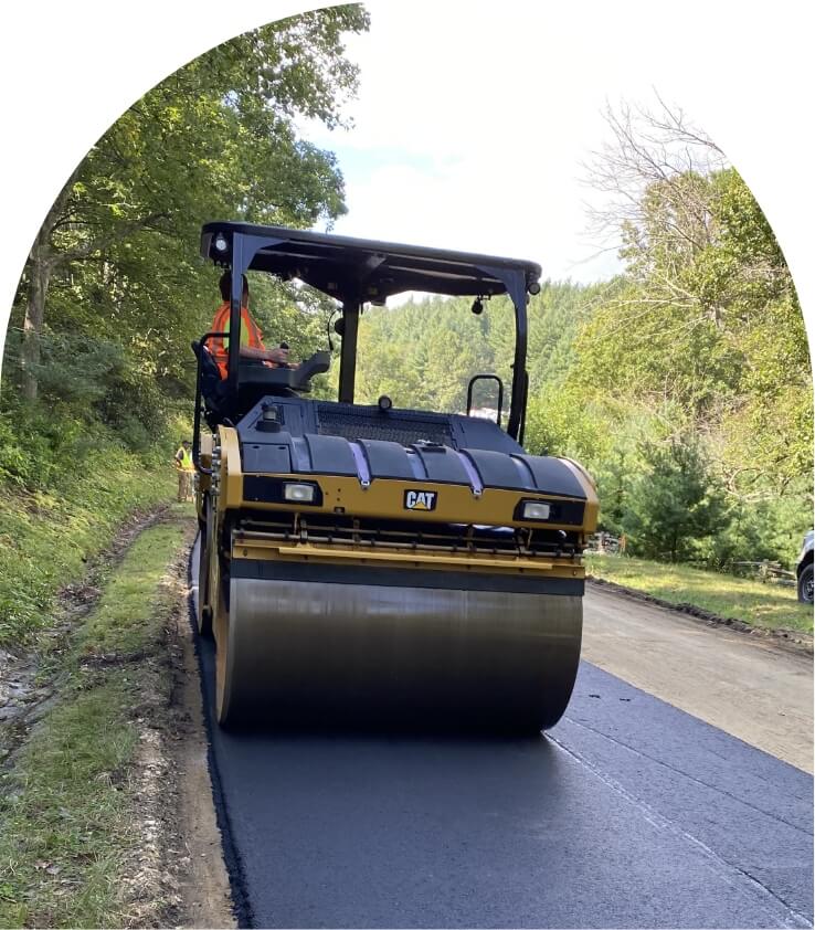 a road roller at work on a paved road in a forested area
