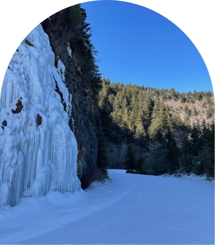 a cliff covered in ice is seen next to a snowy road in the forest
