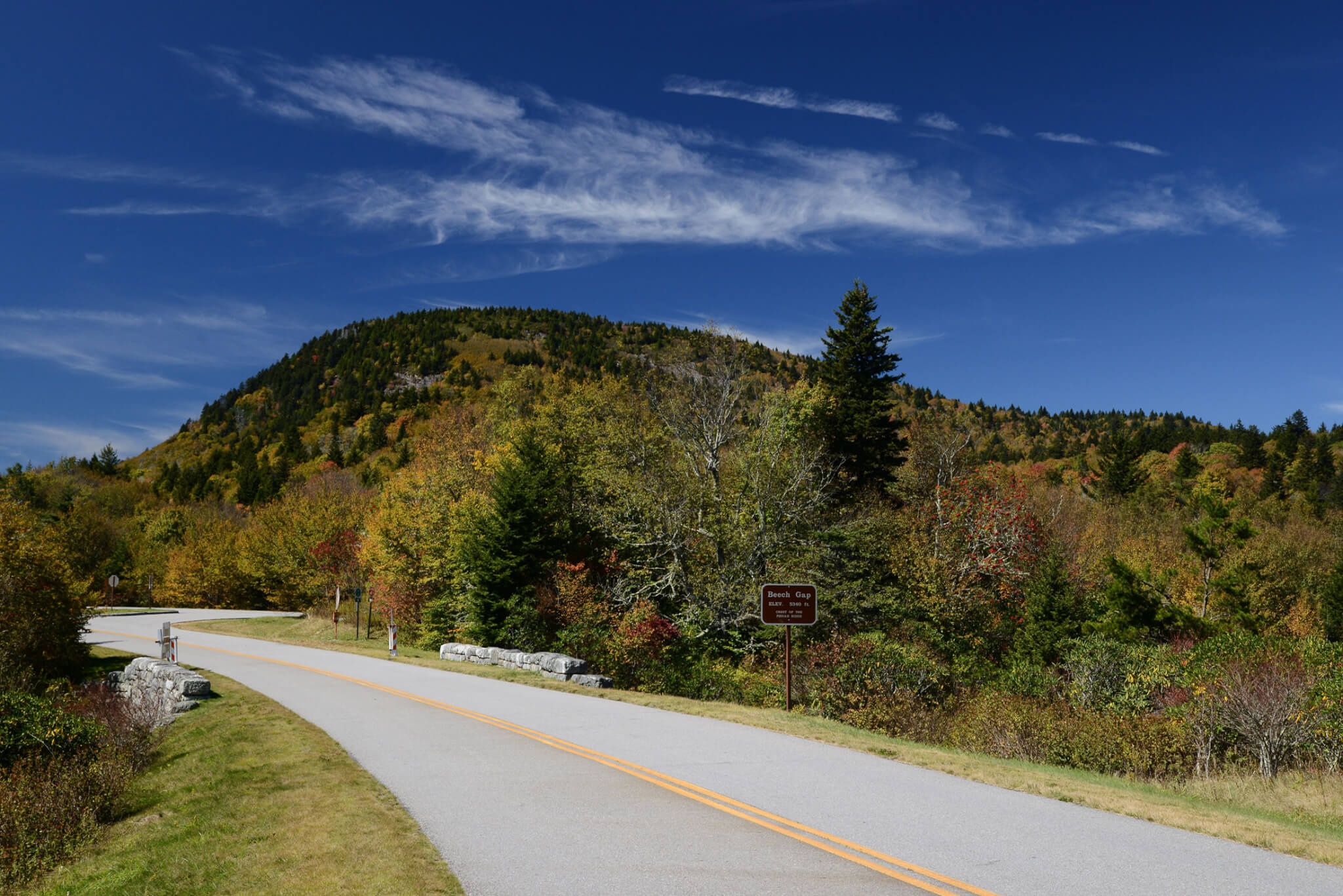 a paved road cuts through mountains that are starting to show fall colors along the blue ridge parkway